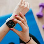 Tracker - Anonymous sportswoman checking smart watch and sitting on mat