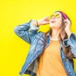 Fashion - Smiling Woman Looking Upright Standing Against Yellow Wall